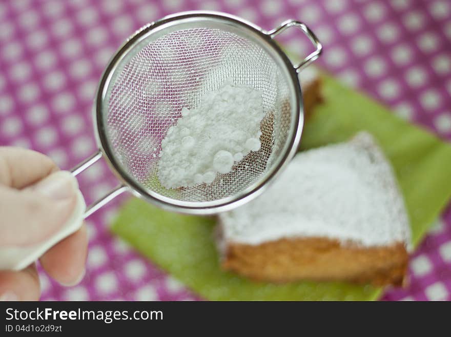 Sieve with powdered sugar and slice of cake