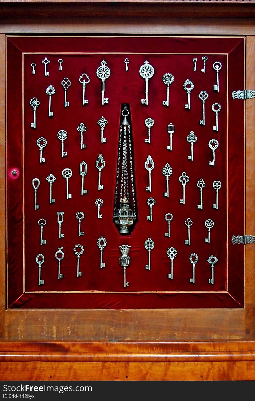 Various sized silver skeleton keys displayed against red velvet in a wood furniture showcase. Various sized silver skeleton keys displayed against red velvet in a wood furniture showcase