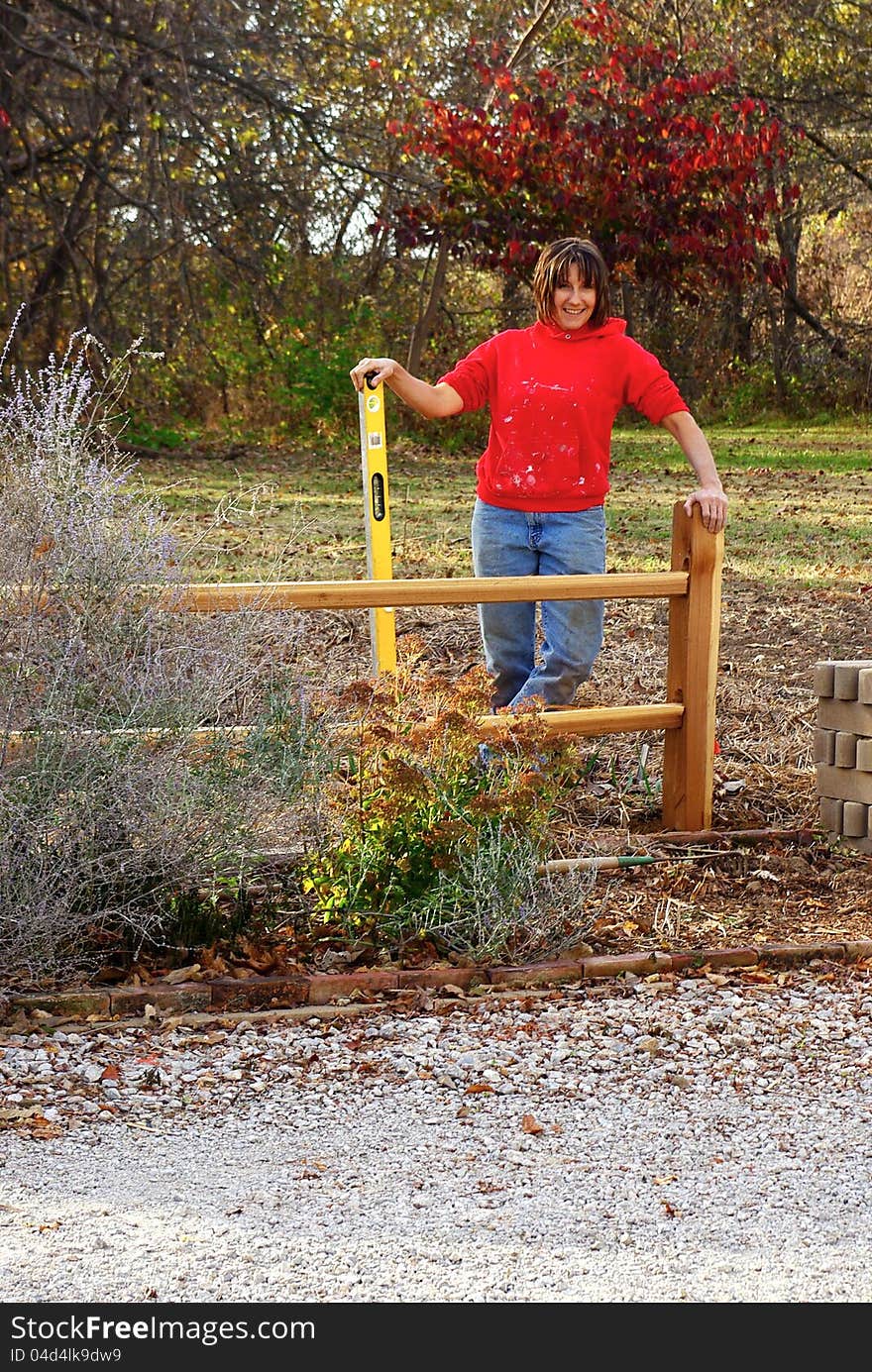 A woman landscaper, level in hand, completes the installation of a split rail fence project. A woman landscaper, level in hand, completes the installation of a split rail fence project