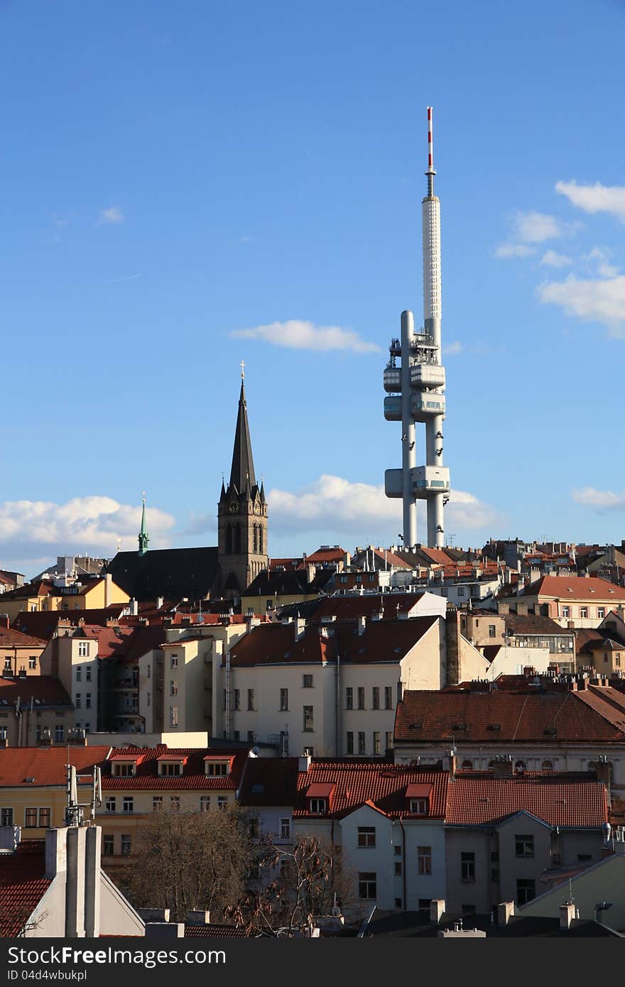 Prague's zizkov transmitter, detail on the church roof and prague, prague houses in the background with a blue sky, blue sky with white clouds above prague, summer day in the streets of prague