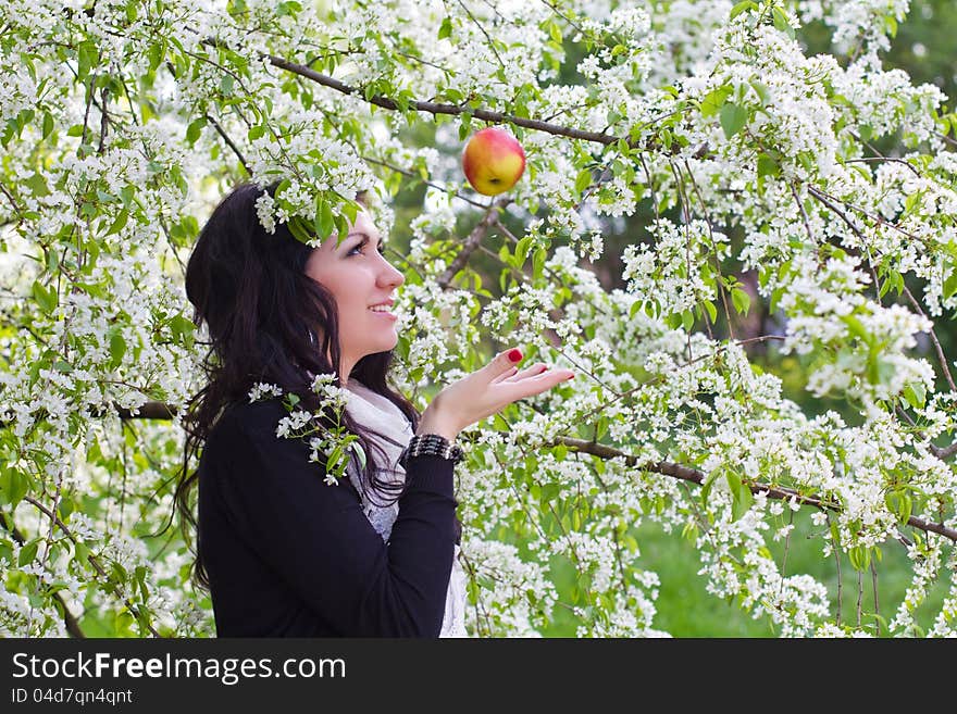 Young woman catching an apple against the backdrop of flowering trees