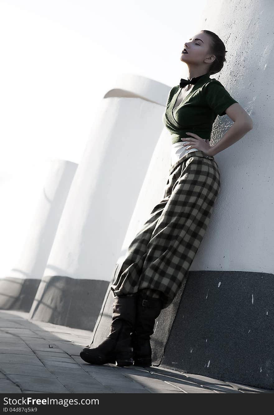 Beautiful young woman in checkered trousers stand leaning on city walls. Beautiful young woman in checkered trousers stand leaning on city walls