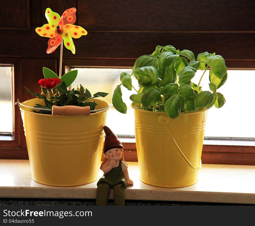 Two buckets containing a rose and basil on a windowsill with a dwarf sitting beside them. Two buckets containing a rose and basil on a windowsill with a dwarf sitting beside them