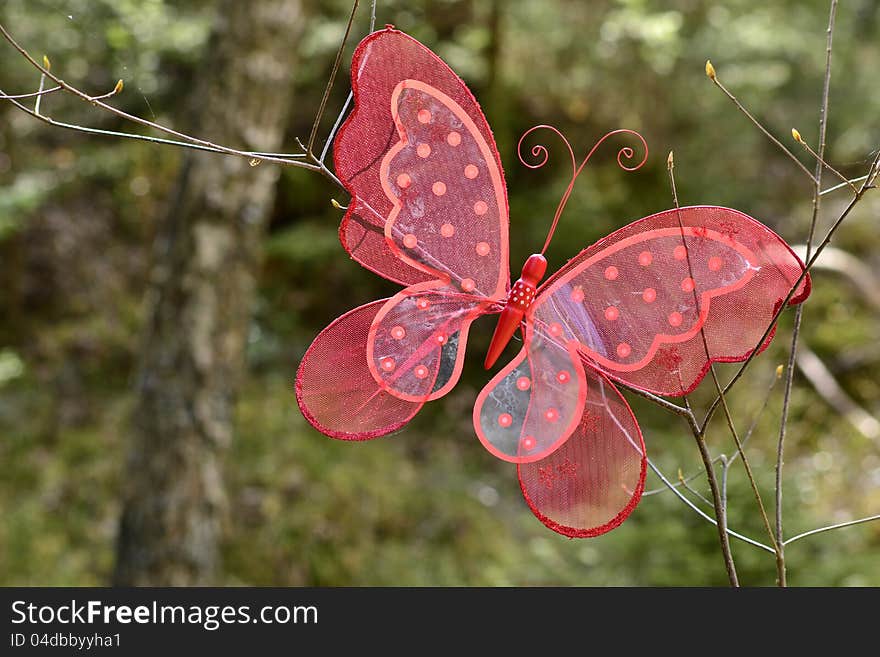 A red decoration butterfly on a branch in the forest. A red decoration butterfly on a branch in the forest.