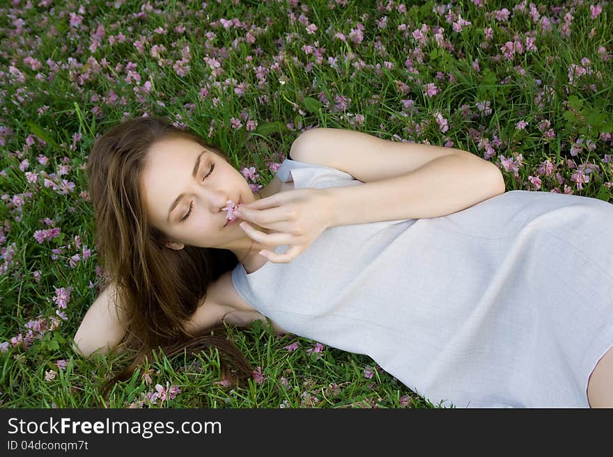 Concept of harmony. Beautiful girl lying on green grass with flowers and holding a flower