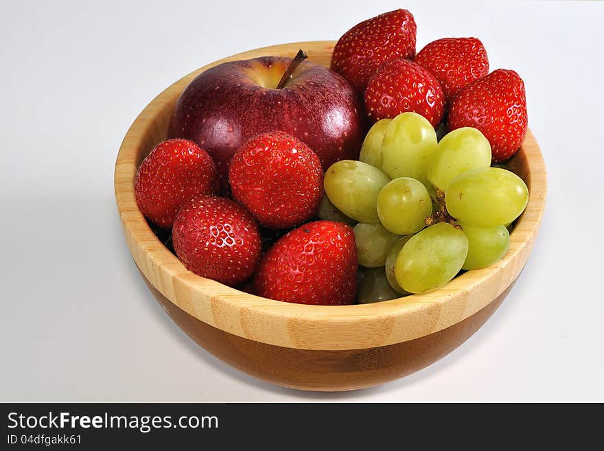 Apple with grapes and strawberries in wooden dish