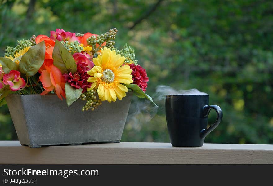 Steaming coffee on front porch next to flower basket. Steaming coffee on front porch next to flower basket