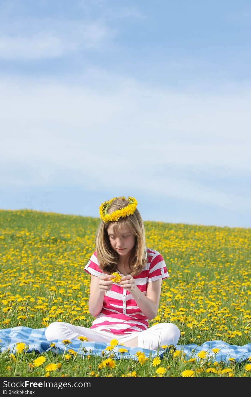 Teenage girl sitting on a dandelion field with a blue sky background