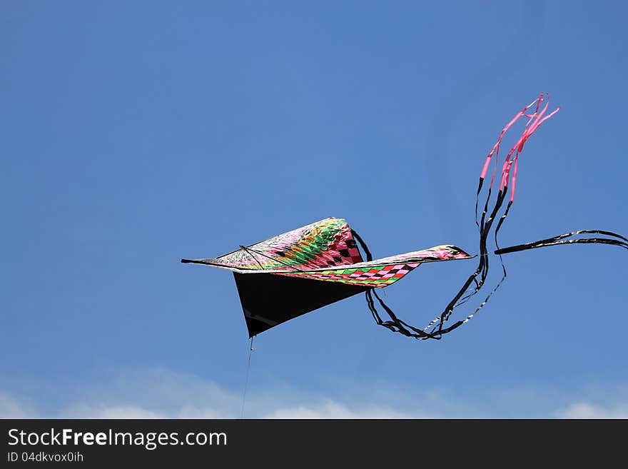 The colorful triangle kite with tail flying in blue sky. The colorful triangle kite with tail flying in blue sky