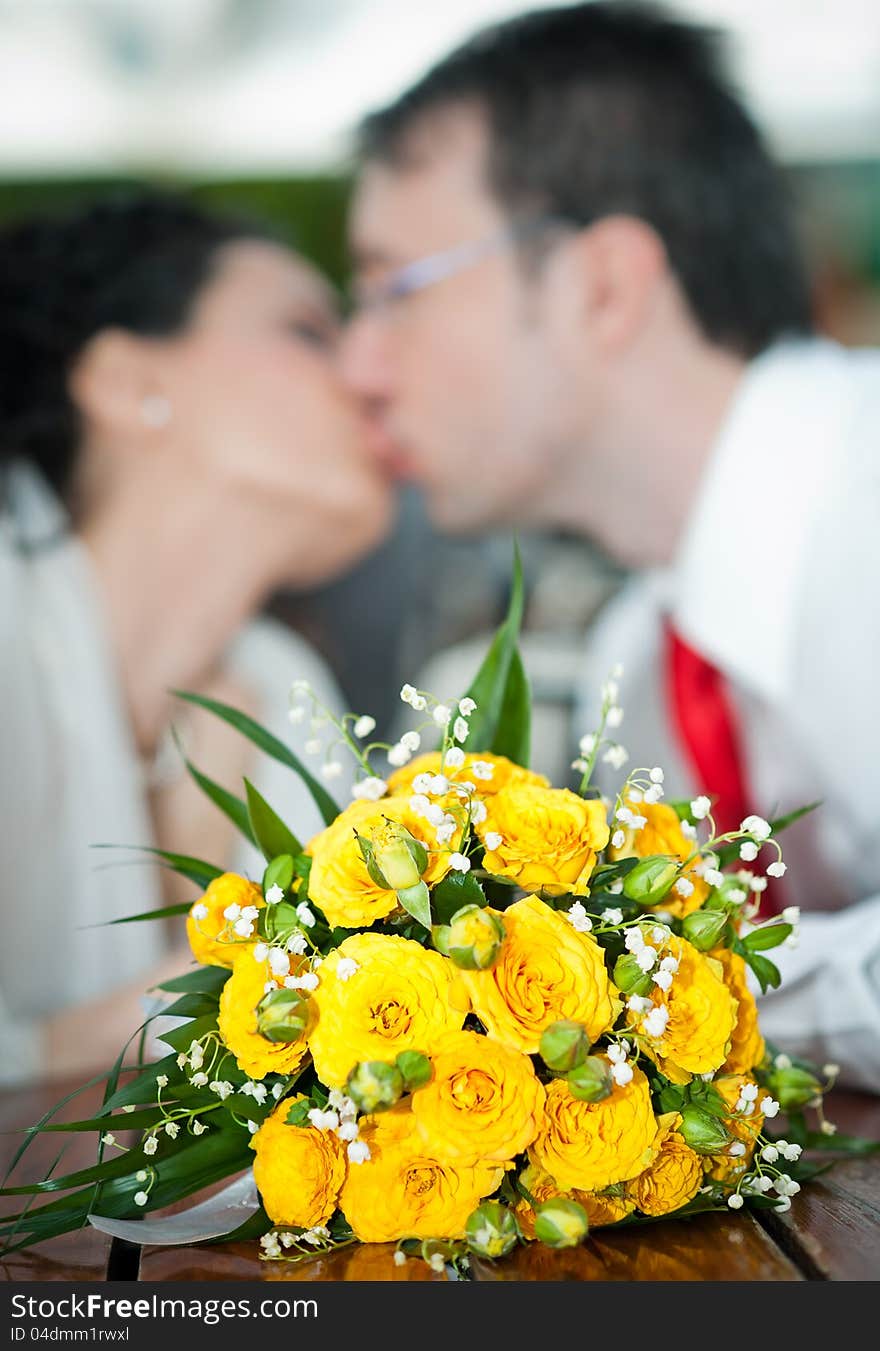 Newly-married couple and wedding bouquet in the foreground. Yellow roses bouquet