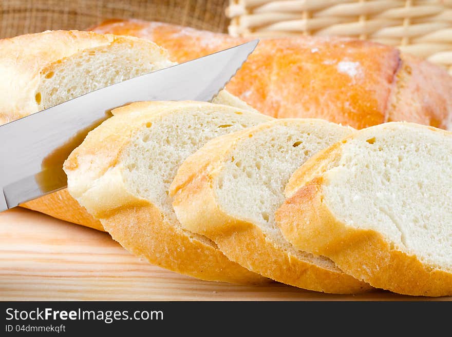 Freshly baked baguette sliced on wooden cutting board, knife. Freshly baked baguette sliced on wooden cutting board, knife