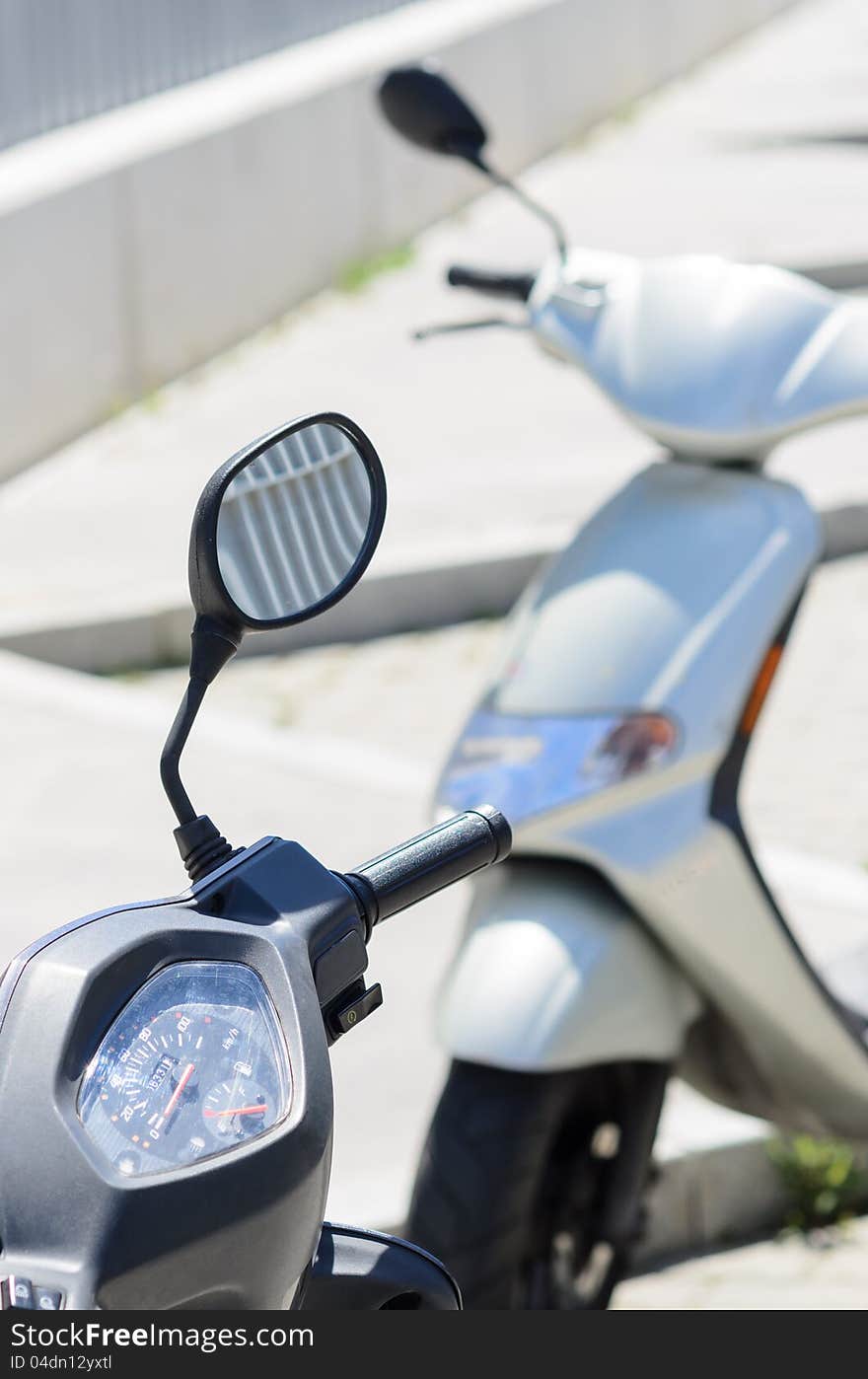 Two motorbikes parked in street, one of them in focus, another out of focus. Two motorbikes parked in street, one of them in focus, another out of focus.