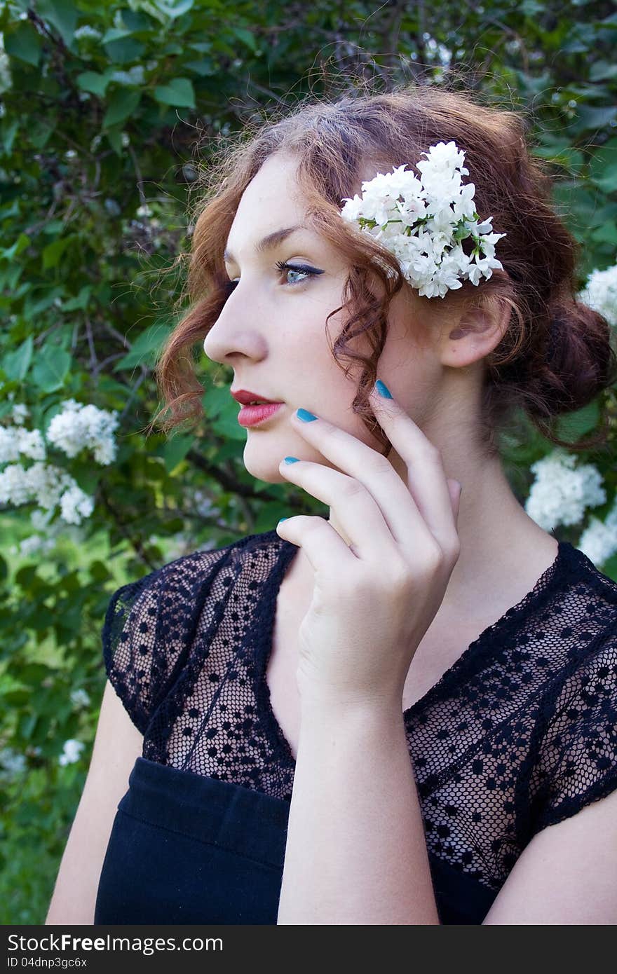 Portrait of a beautiful girl with white lilacs on his head looking to the distance