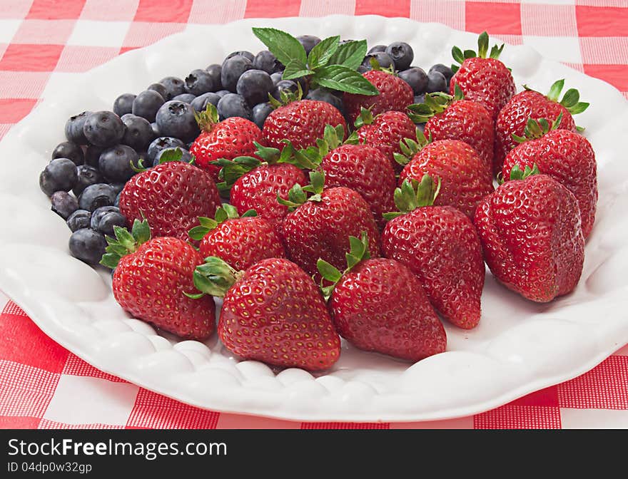 Luscious nutritious strawberries and blueberries arranged on white plate on checkered cloth. Luscious nutritious strawberries and blueberries arranged on white plate on checkered cloth.