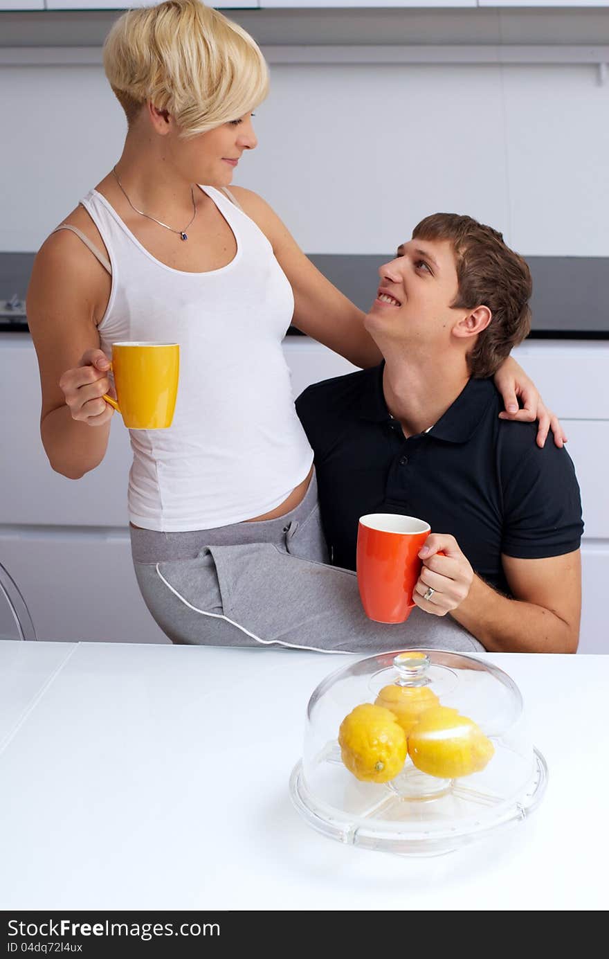 Portrait of a happy couple posing in the kitchen with cups and lemons on the table