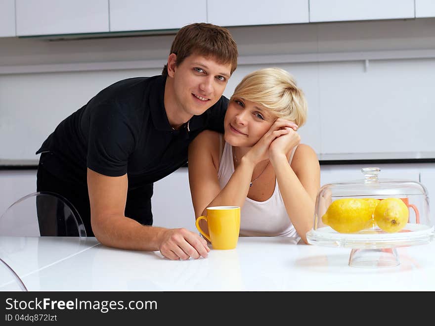 Portrait of a happy couple posing in the kitchen with cups and lemons on the table