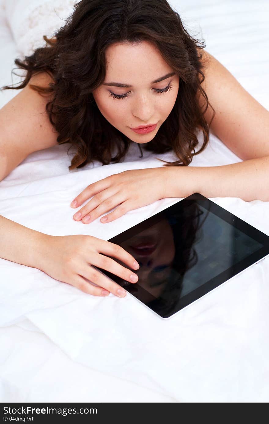 Beautiful emotional young woman using tablet computer in her bedroom high key. Beautiful emotional young woman using tablet computer in her bedroom high key