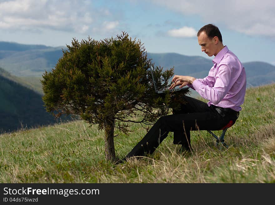 Man works on computer, located on tree. Man works on computer, located on tree