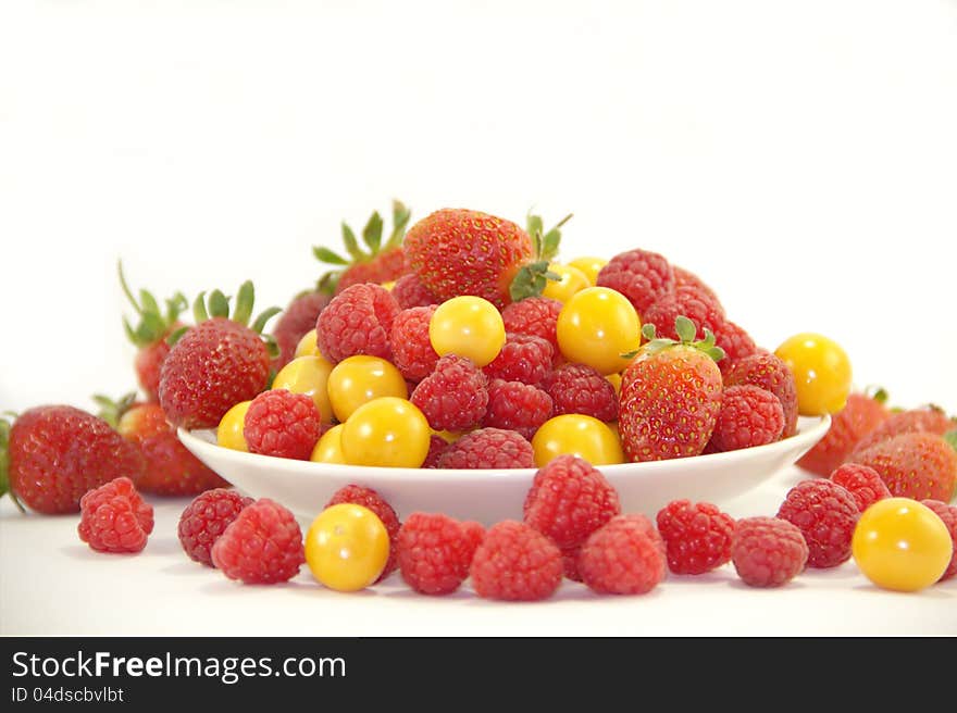 Fresh raspberries, strawberries and gooseberries on the plate on white background