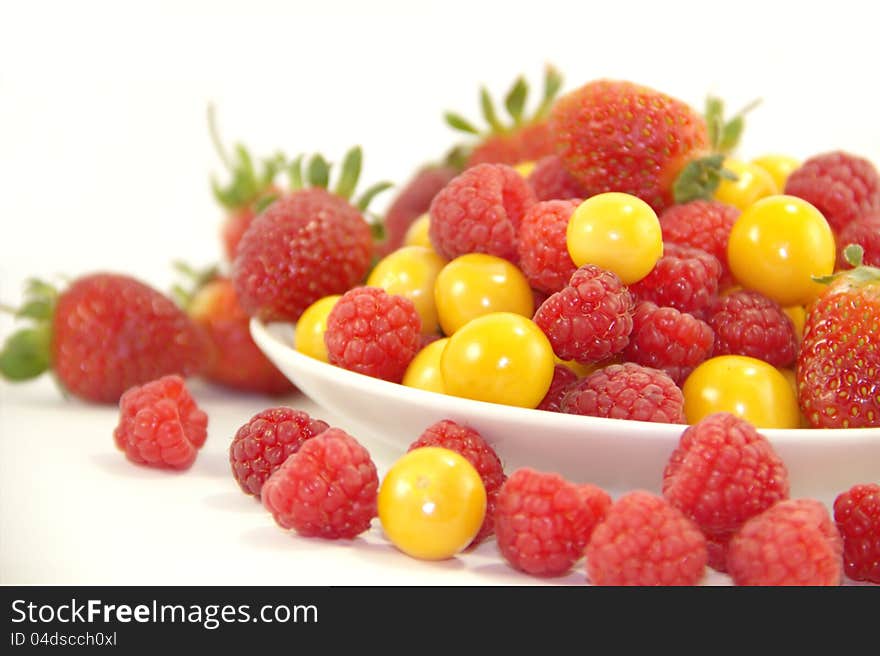 Raspberries, gooseberries and strawberries on the plate on white background