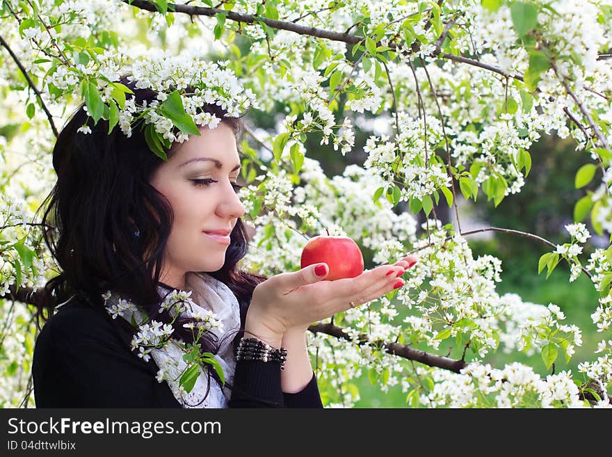 Young woman holding apple against the backdrop of flowering trees