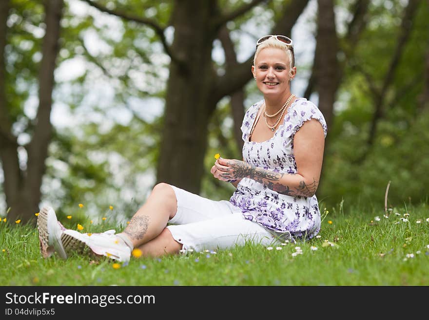 Beautiful tattooed woman with a floret in her hands sits on the meadow. Beautiful tattooed woman with a floret in her hands sits on the meadow