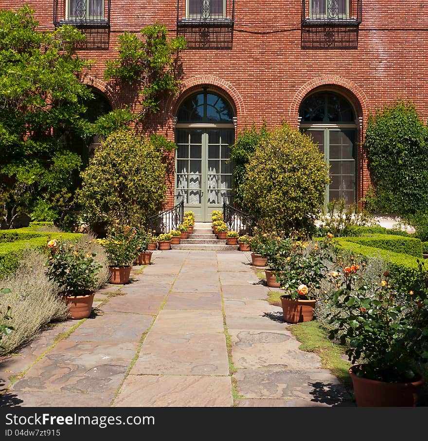 Red brick building with French door opening toward the garden. Beautiful flowers in pots on each side of the stairs. Red brick building with French door opening toward the garden. Beautiful flowers in pots on each side of the stairs