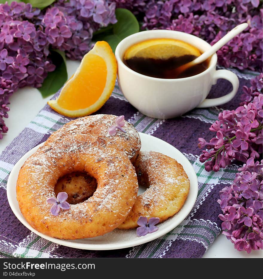 Sweet cottage cheese donuts with orange tea for breakfast and lilac flowers on the table. Sweet cottage cheese donuts with orange tea for breakfast and lilac flowers on the table