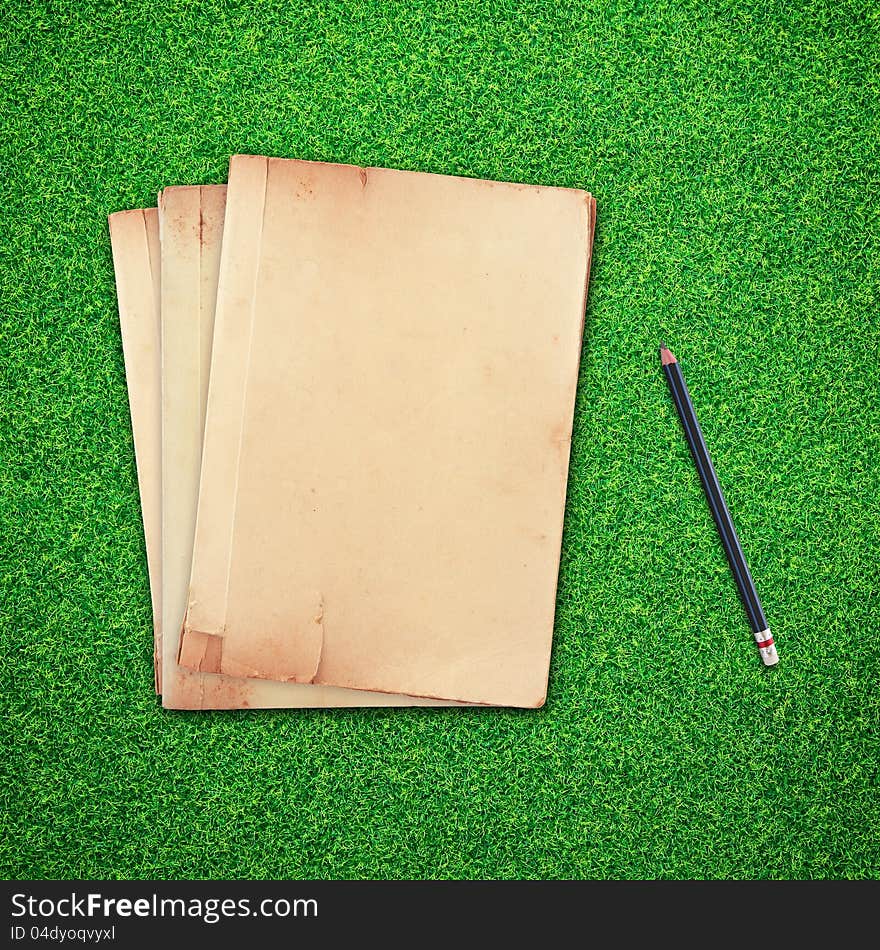 Pencil and old book on green grass background