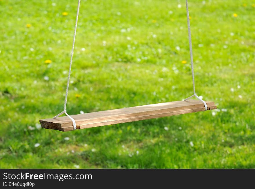 An empty wooden swing in the garden in summer