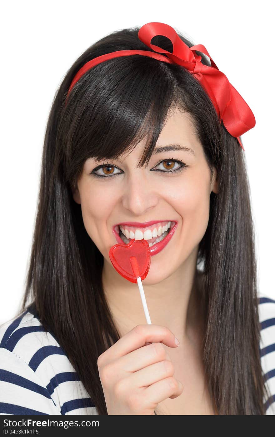 Young retro girl biting a red heart shape lollipop. she is brunete, and is smiling wears a red bow in her hair. Young retro girl biting a red heart shape lollipop. she is brunete, and is smiling wears a red bow in her hair.