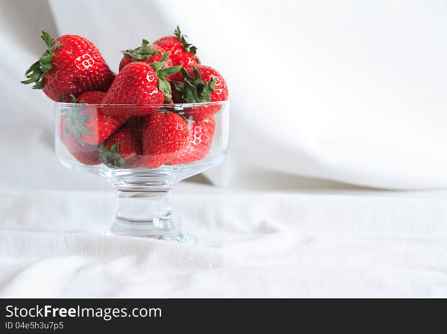 Transparent glass vase full of red strawberries on white textile background with free space for text. Transparent glass vase full of red strawberries on white textile background with free space for text