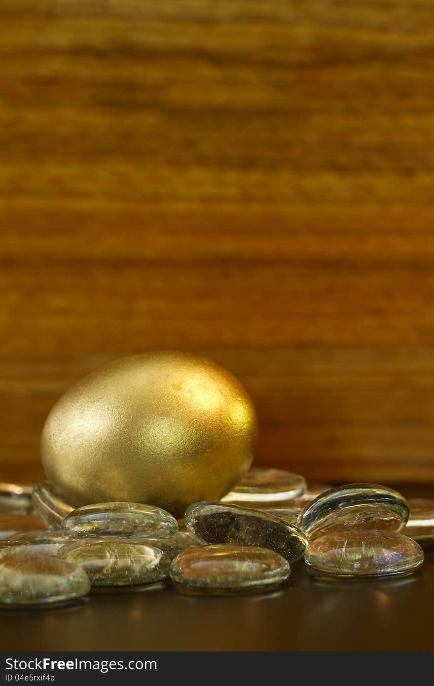 Gold egg glistens on glass stones in front of wood grain background; vertical image with copy space at top;. Gold egg glistens on glass stones in front of wood grain background; vertical image with copy space at top;