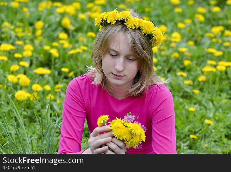 Happy girl in a wreath from yellow dandelions admires flowers. Happy girl in a wreath from yellow dandelions admires flowers