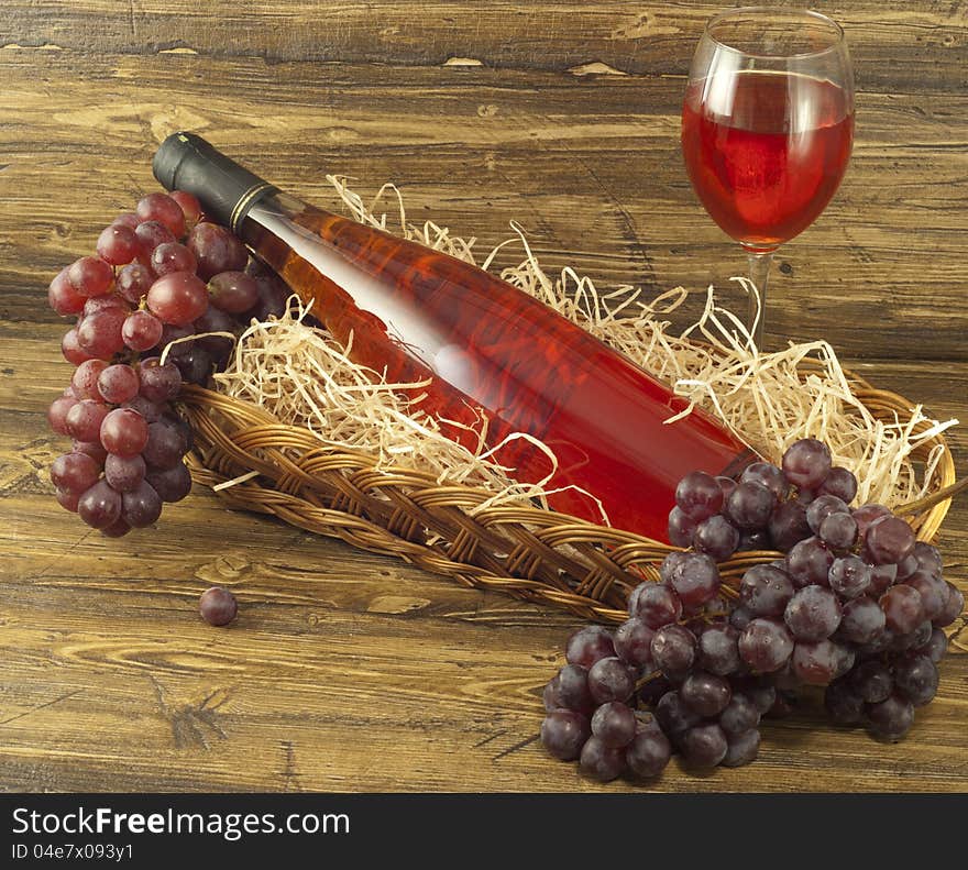 Bottle of pink wine in a basket and fresh grapes on a table. Bottle of pink wine in a basket and fresh grapes on a table.