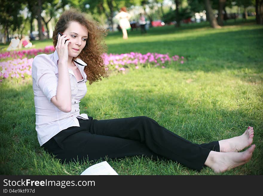 Curly-haired girl with the phone sitting on the grass in the summer