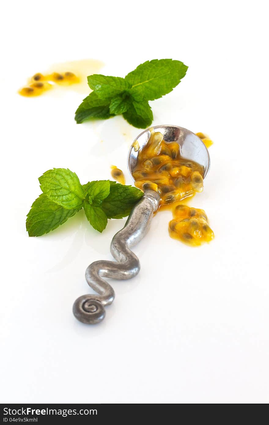 Granadilla pulp on a silver spoon with mint and isolated on a white backround