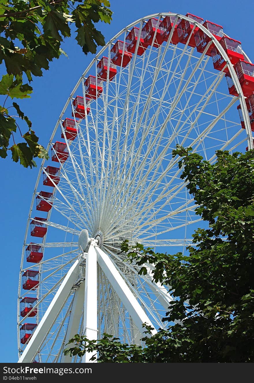 A high Ferris wheel amusement ride at Navy Pier Chicago, IL with trees in foreground. A high Ferris wheel amusement ride at Navy Pier Chicago, IL with trees in foreground