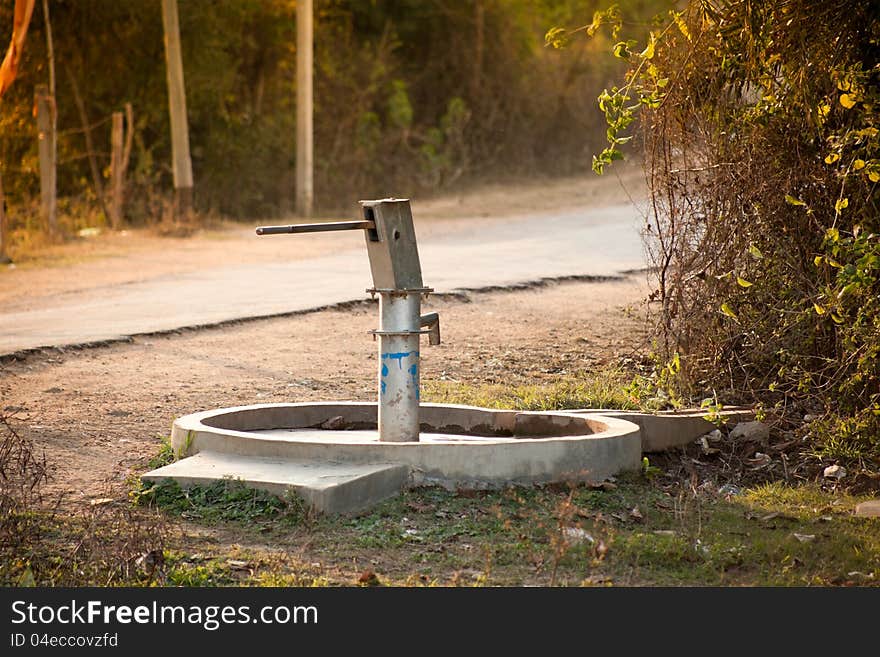 Old hand operated water pump standing on road side in the forest