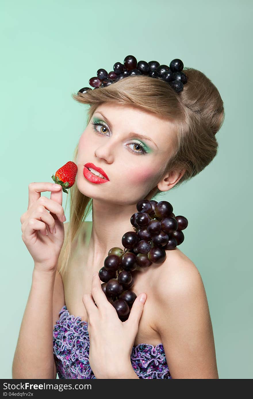 Young woman with strawberry and bunch of grapes, on green background