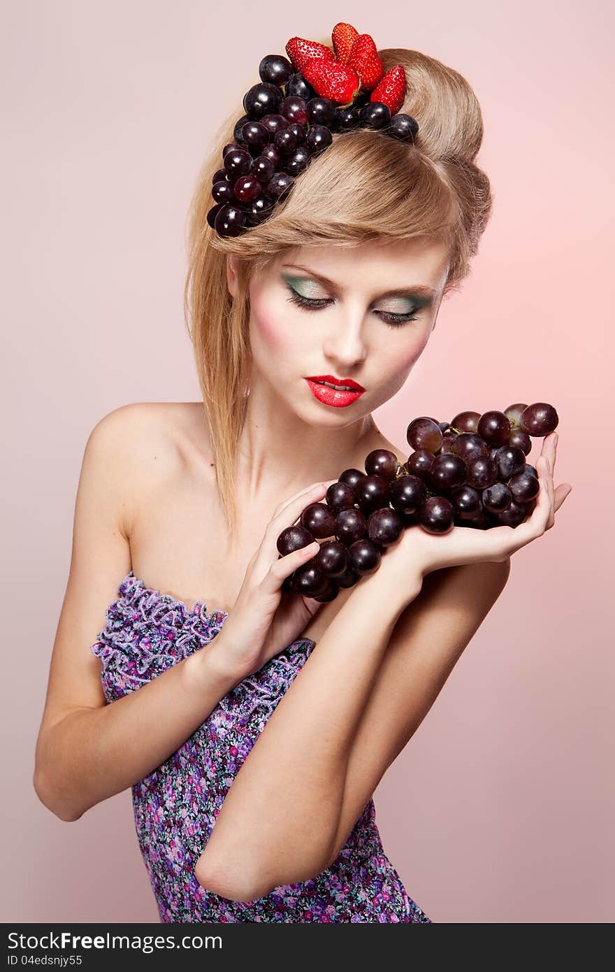 Young woman with strawberry and bunch of grapes in her hairs, on pink background