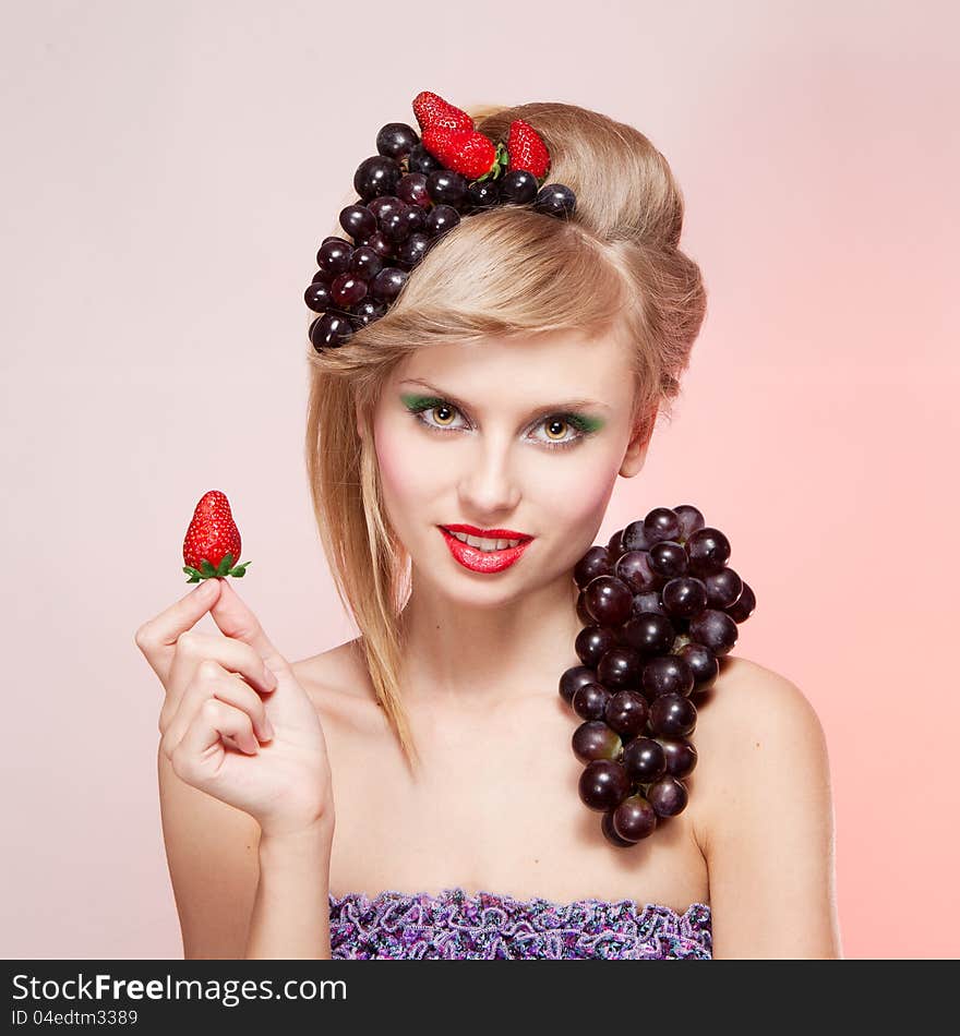 Young woman with strawberries and bunch of grapes holding a strawberry