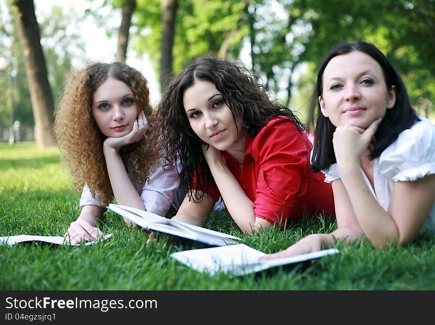 Portrait of three friends studying on the grass in the park