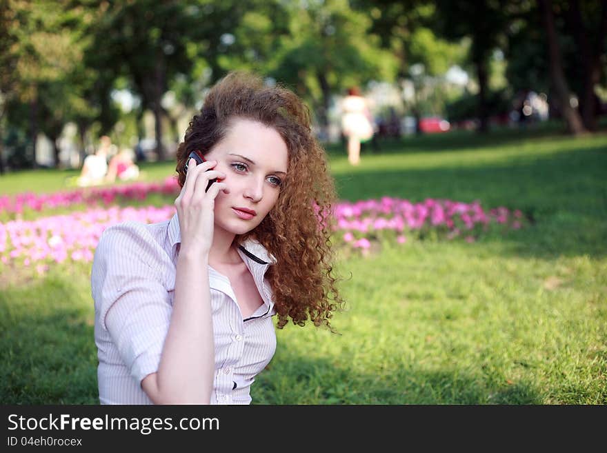 Cute curly girl talking on the phone in the park