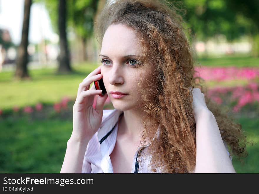 Portrait of a pretty girl with curly phone in park