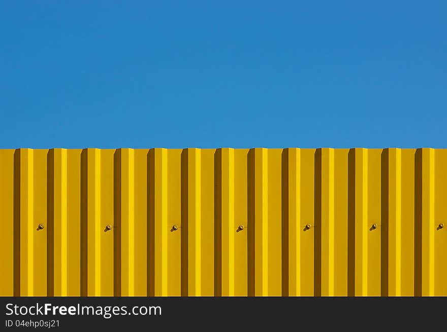 Fence made of corrugated yellow against the blue sky. It looks like a flag of Ukraine. Fence made of corrugated yellow against the blue sky. It looks like a flag of Ukraine