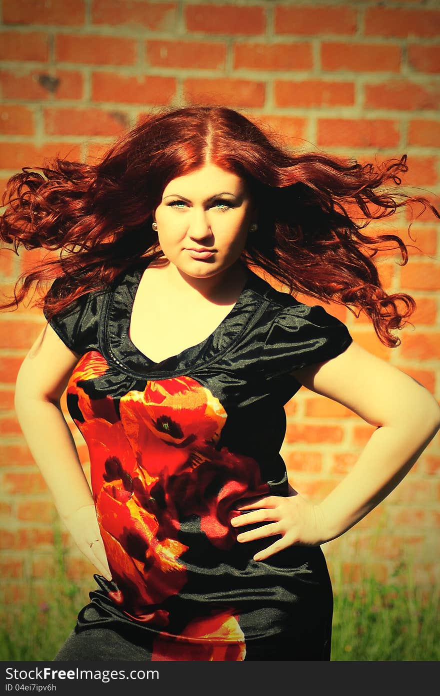 Beautiful young redhead woman with flying long hair on the background of a red brick wall. Beautiful young redhead woman with flying long hair on the background of a red brick wall