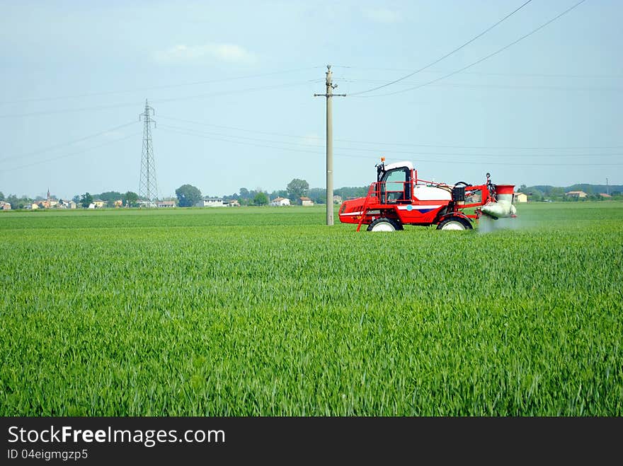 Red tractor waters a cultivated field in farmlands