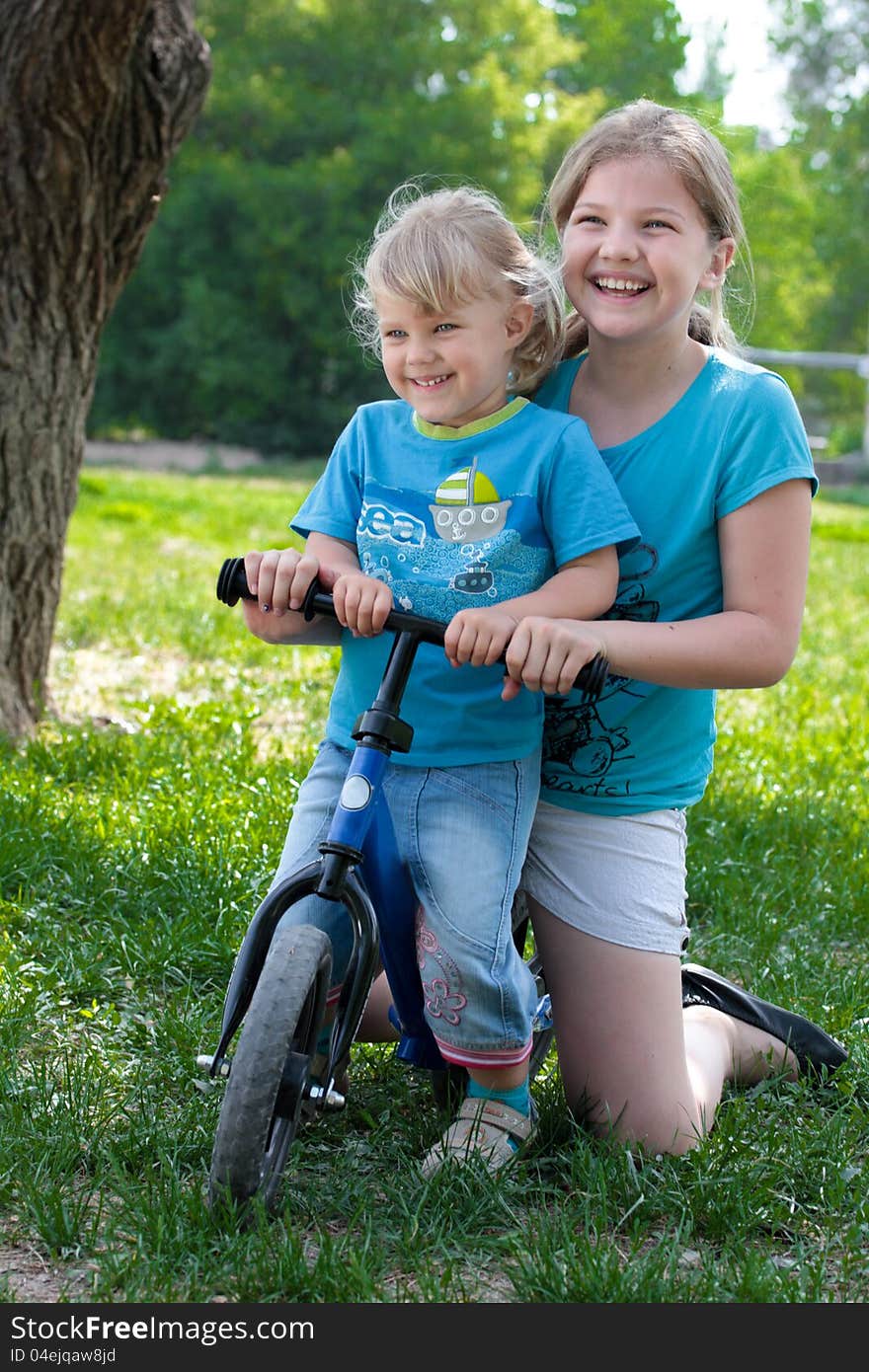 Two sisters sitting on a small bike and laughing. Two sisters sitting on a small bike and laughing