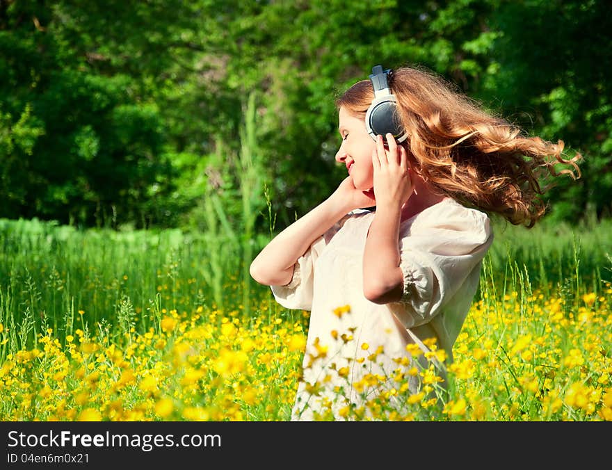 Beautiful girl in headphones enjoying the music with flowing hair in a field of flowers in nature. Beautiful girl in headphones enjoying the music with flowing hair in a field of flowers in nature